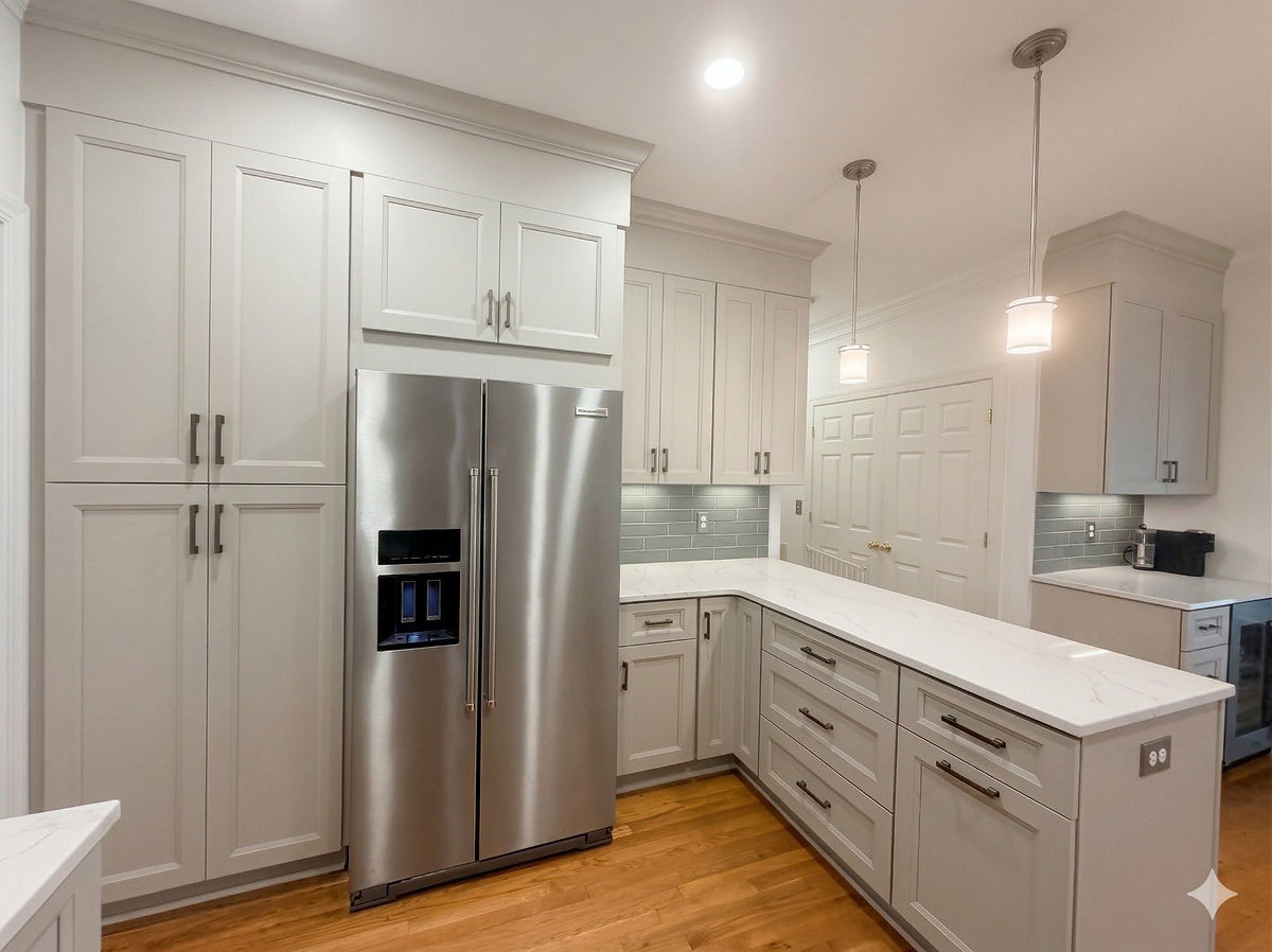 Modern kitchen with stainless steel fridge, white cabinets, and marble countertops. Wooden floor, pendant lights, calm ambiance for this home renovation near Huntersville, NC.