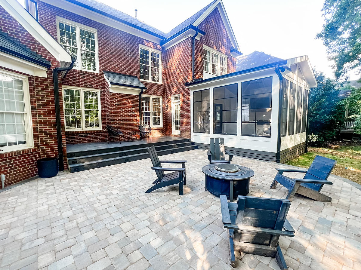 home renovation near Cornelius, NC featuring new patio with gray paver stone, black Adirondack chairs around a fire pit and black decking with more chair and tables in the background.