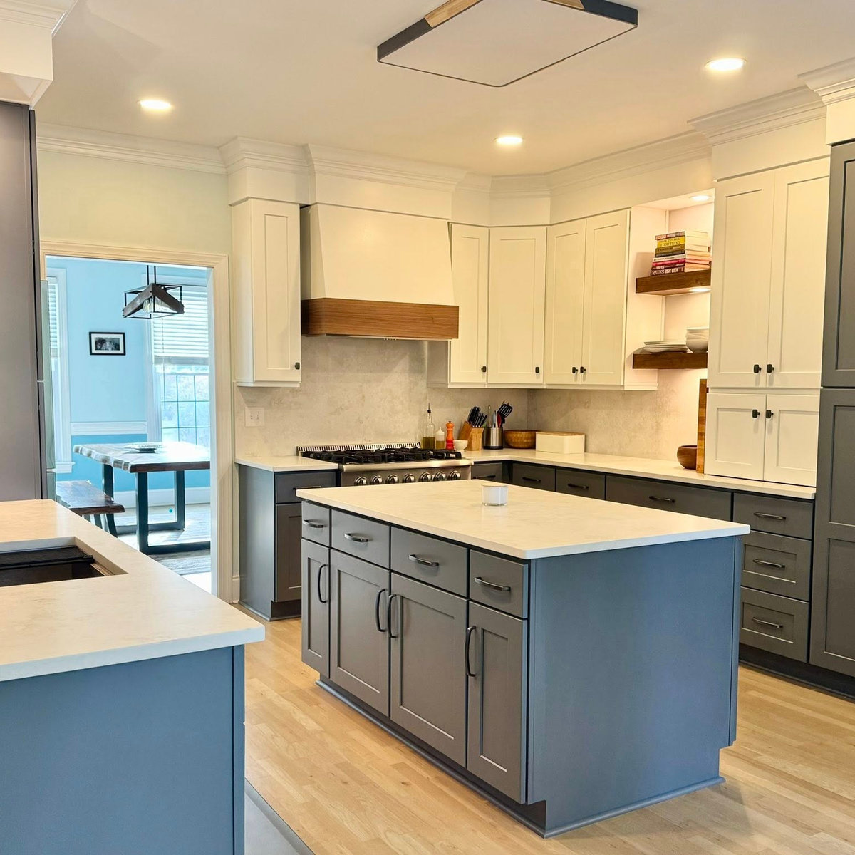 side angle of the renovated kitchen with blue cabinetry, light hardwood floors, light stone counters, and black hardware