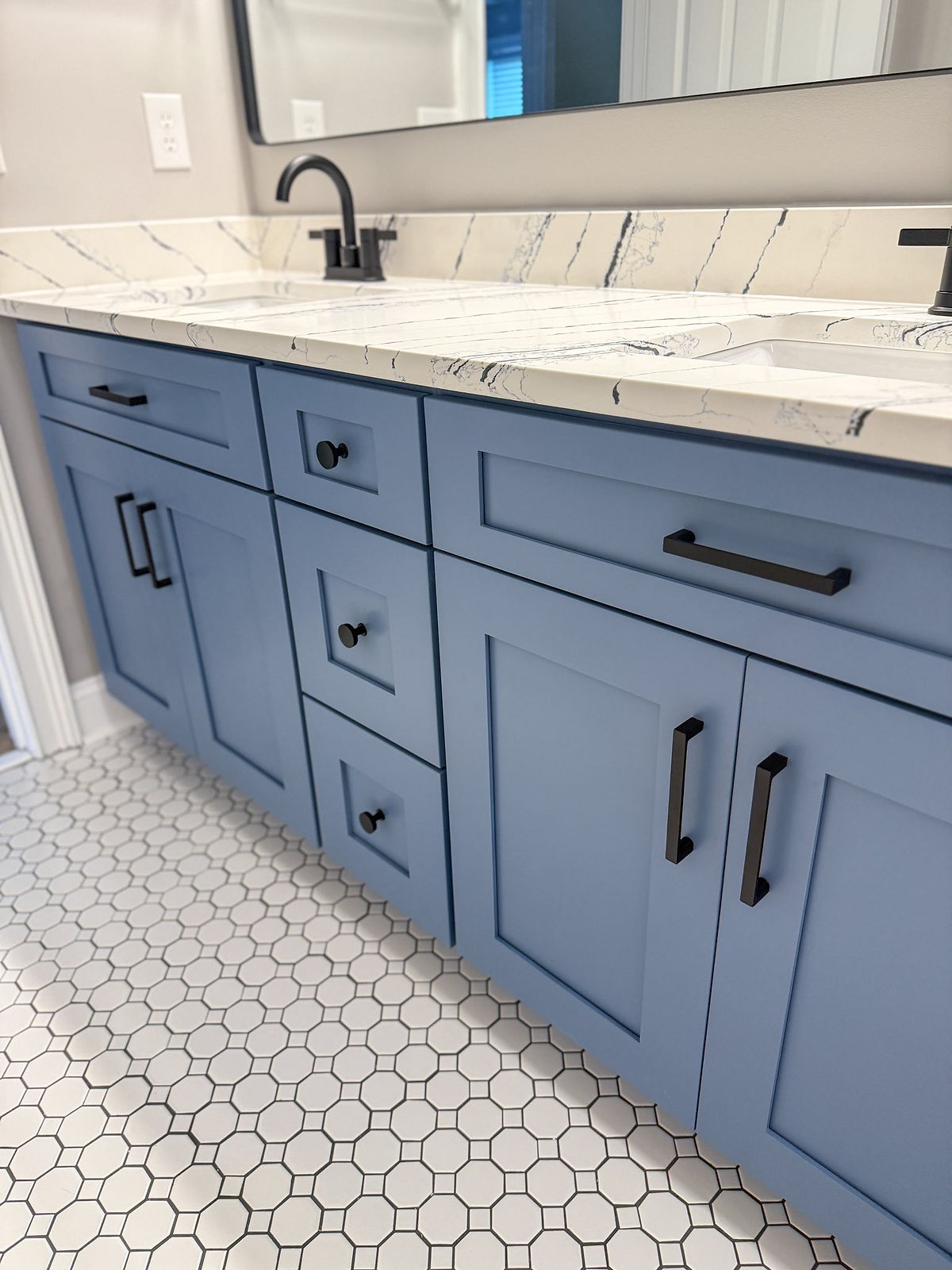 home renovation near Cornelius, NC featuring blue cabinetry one a double vanity with black hardware and a curved black metal frame mirror above the sinks