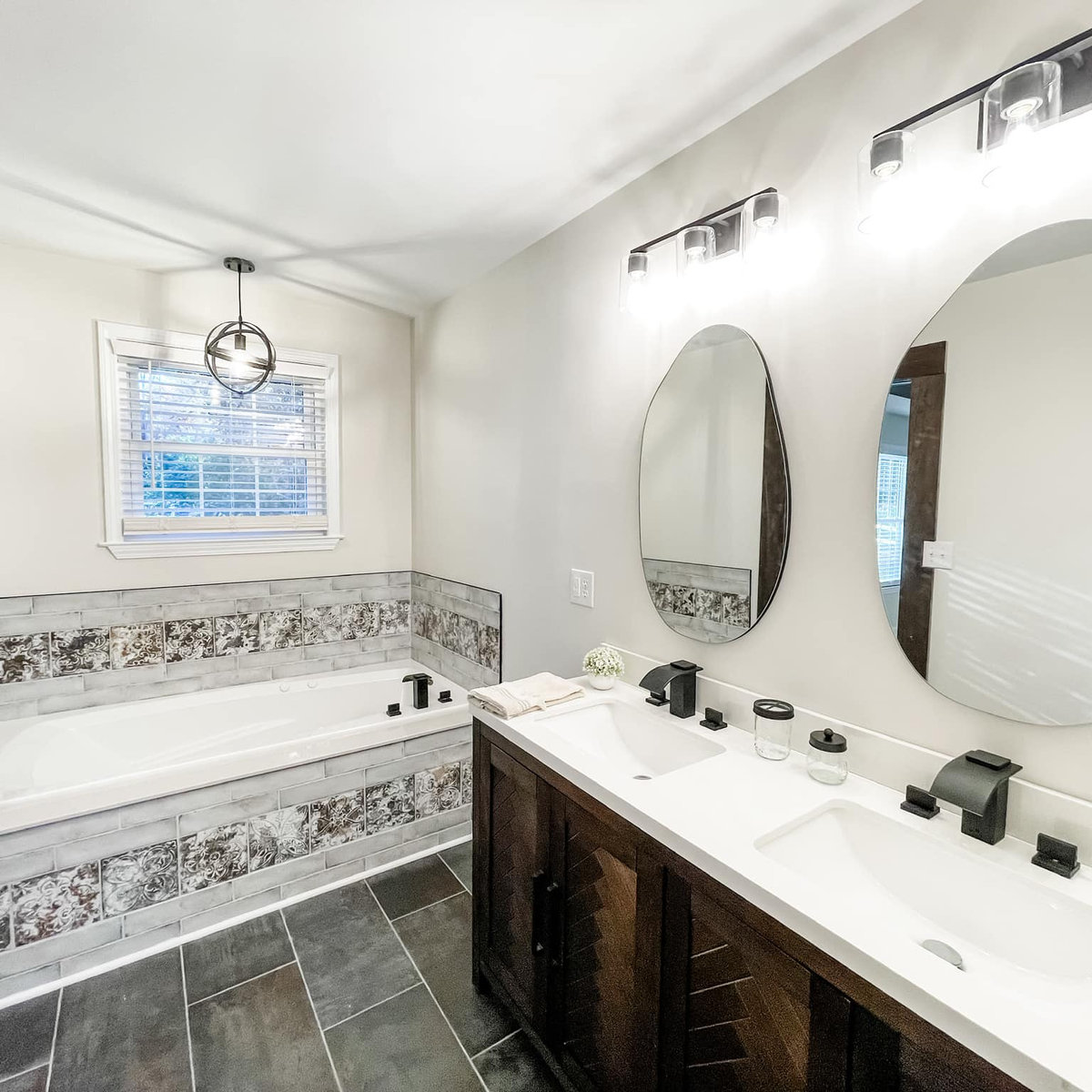 renovated bathroom with decorative tiled tub, double vanity, and dark tiled floors