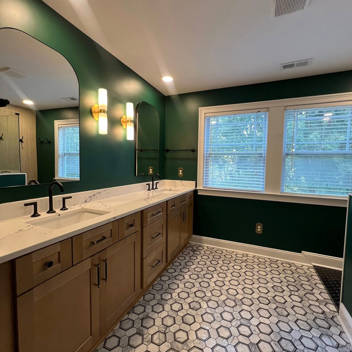 wide angle shot of dark green bathroom with decorative tile floors, wooden vanity, and white counter tops