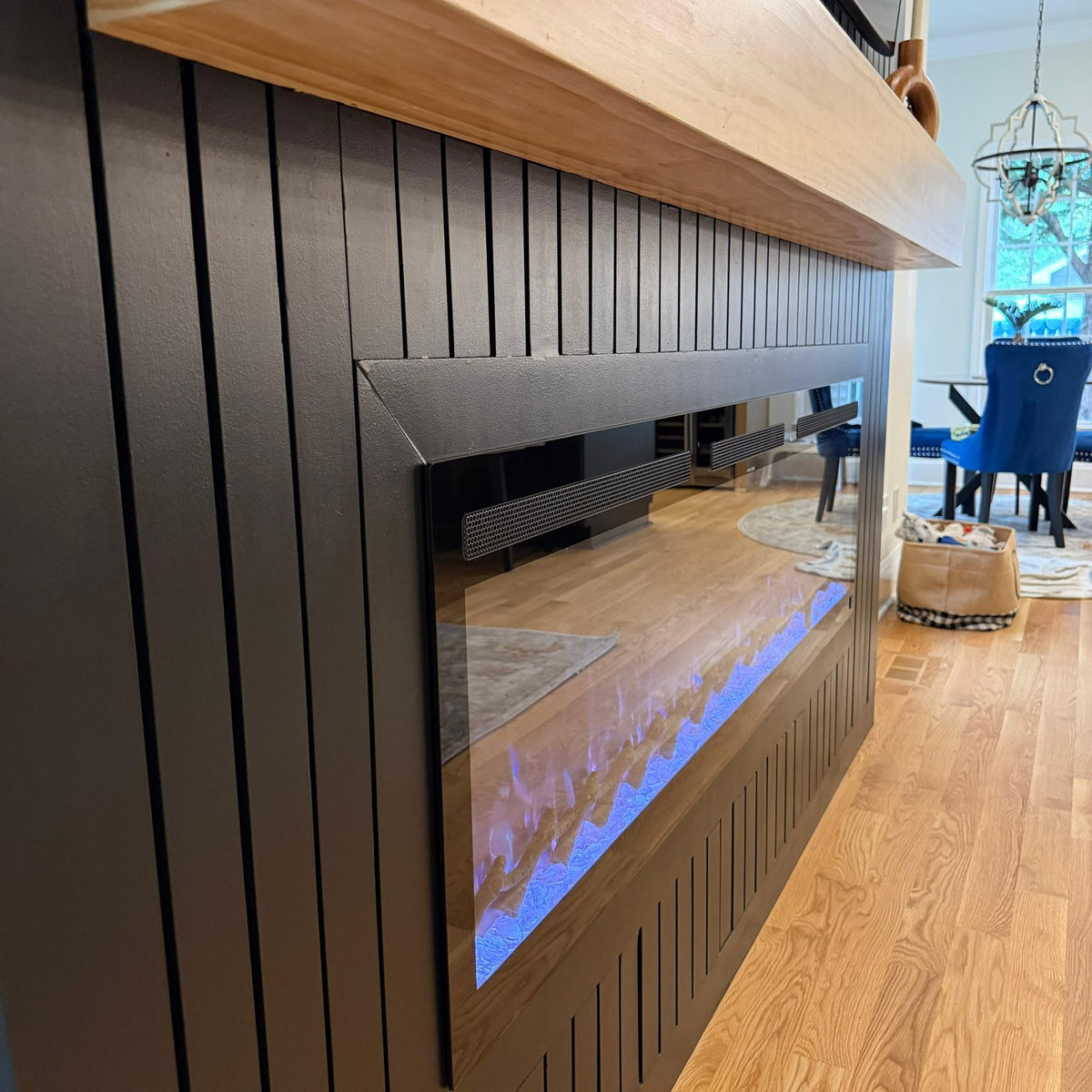 side view of black textured media wall, electric fireplace with blue flames, and wooden mantel