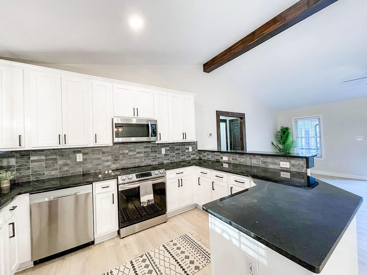 renovated kitchen with black granite counters, white cabinetry, and gray tile backsplash.