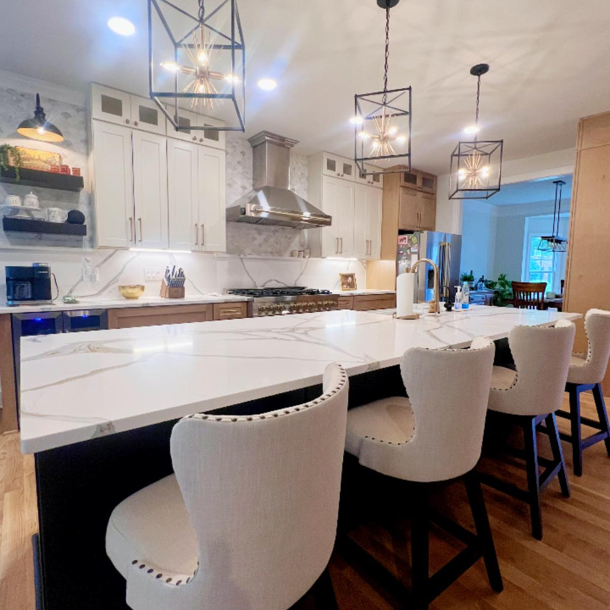 large kitchen island with light stone counters, modern farmhouse style pendant lights above and light upholstered bar stools in the foreground