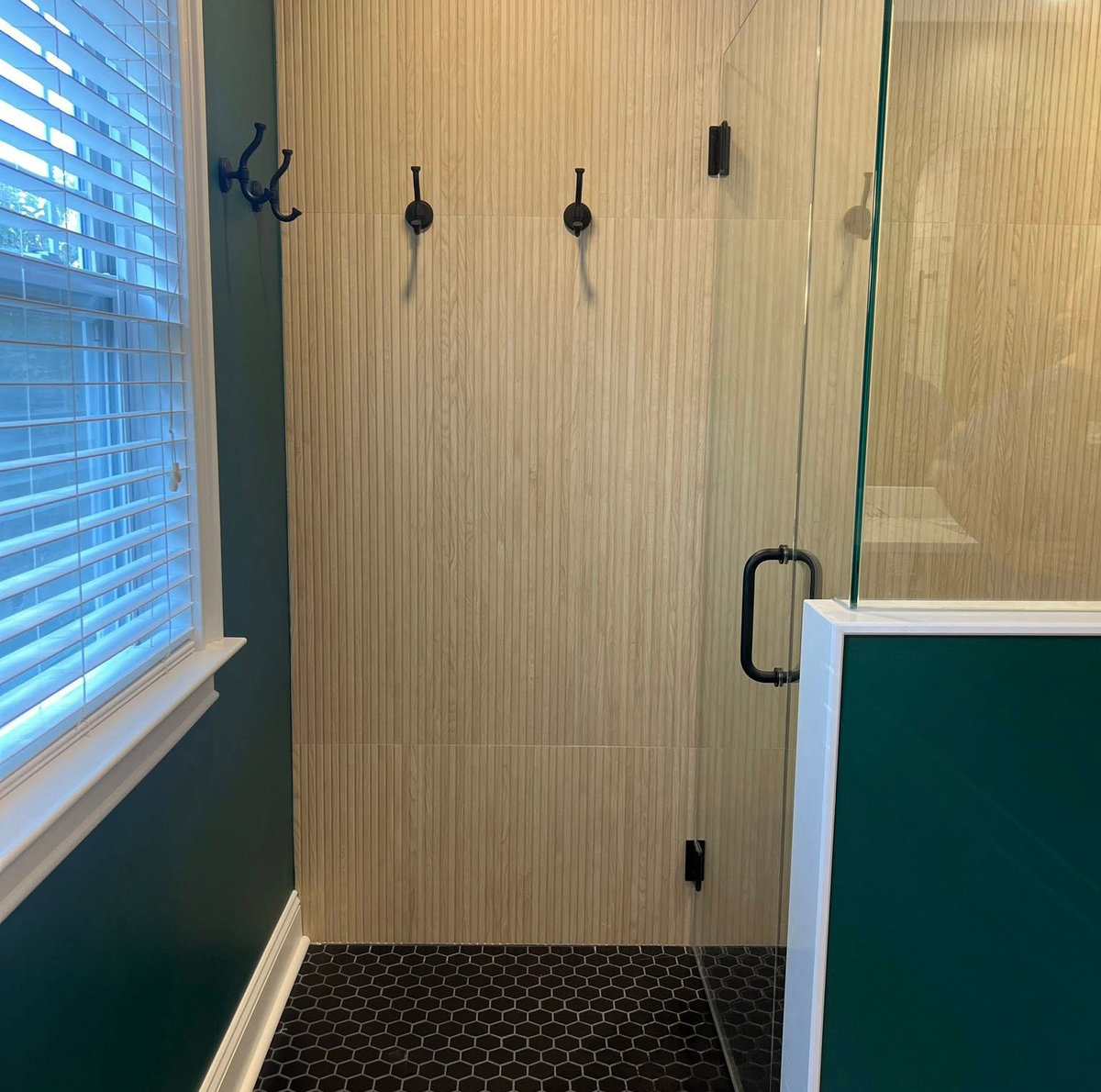 dark green wall with a window and white trim, glass shower door is to the right