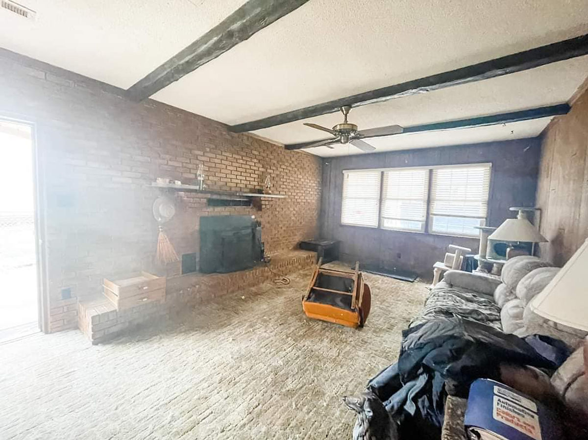 dated living room with carpet, brick accent wall, and wood beams on ceiling