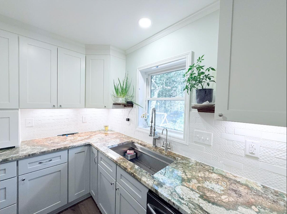 Bright kitchen with white cabinets, granite countertops, plants, and a window. Soft lighting creates a clean, refreshing atmosphere.