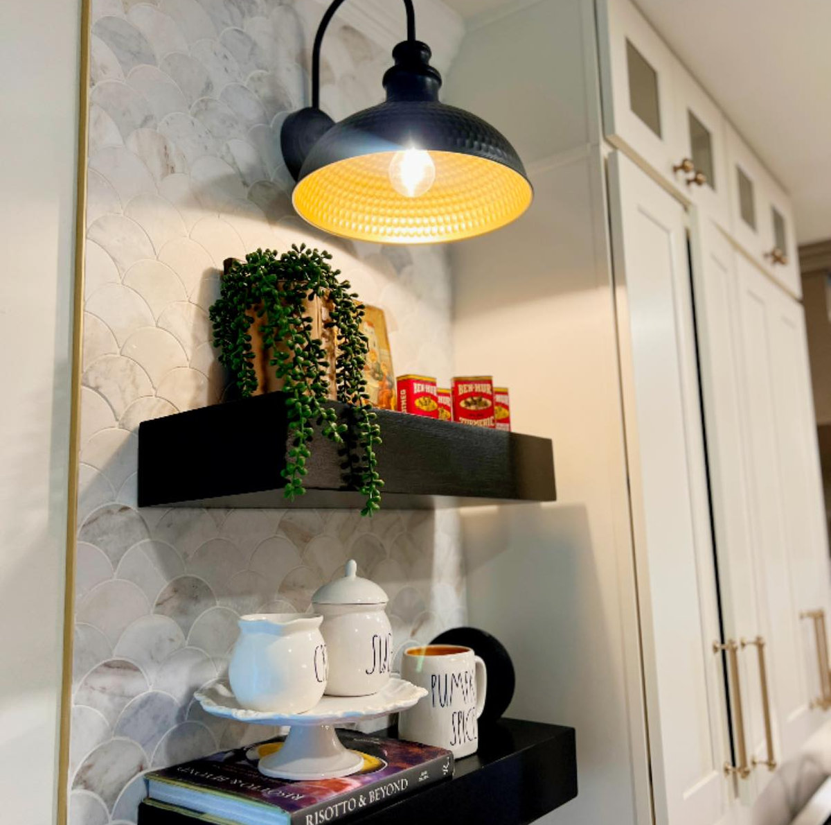 a marble tiled wall behind open dark shelves with a black farmhouse sconce above