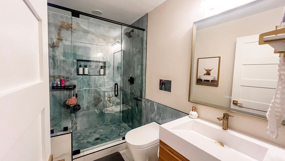 home renovation near Cornelius, NC featuring renovated bathroom with white walls and blue decorative tiled shower stall. White vanity with wooden drawers in the foreground.