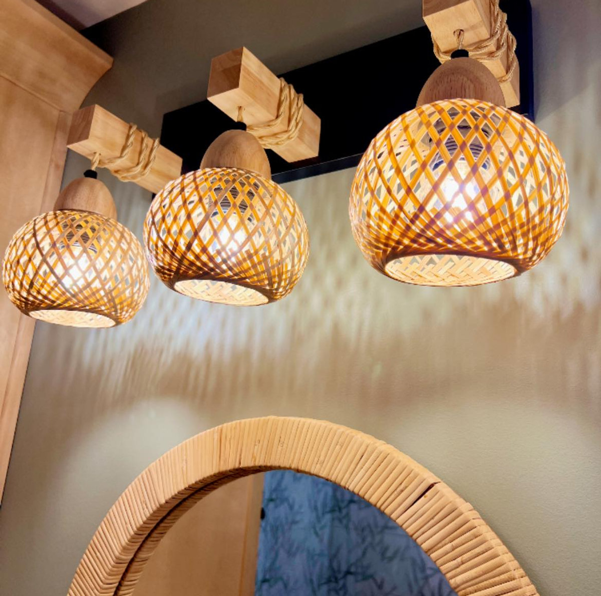 rattan wrapped mirror on a green wall beneath three rattan wrapped light shades