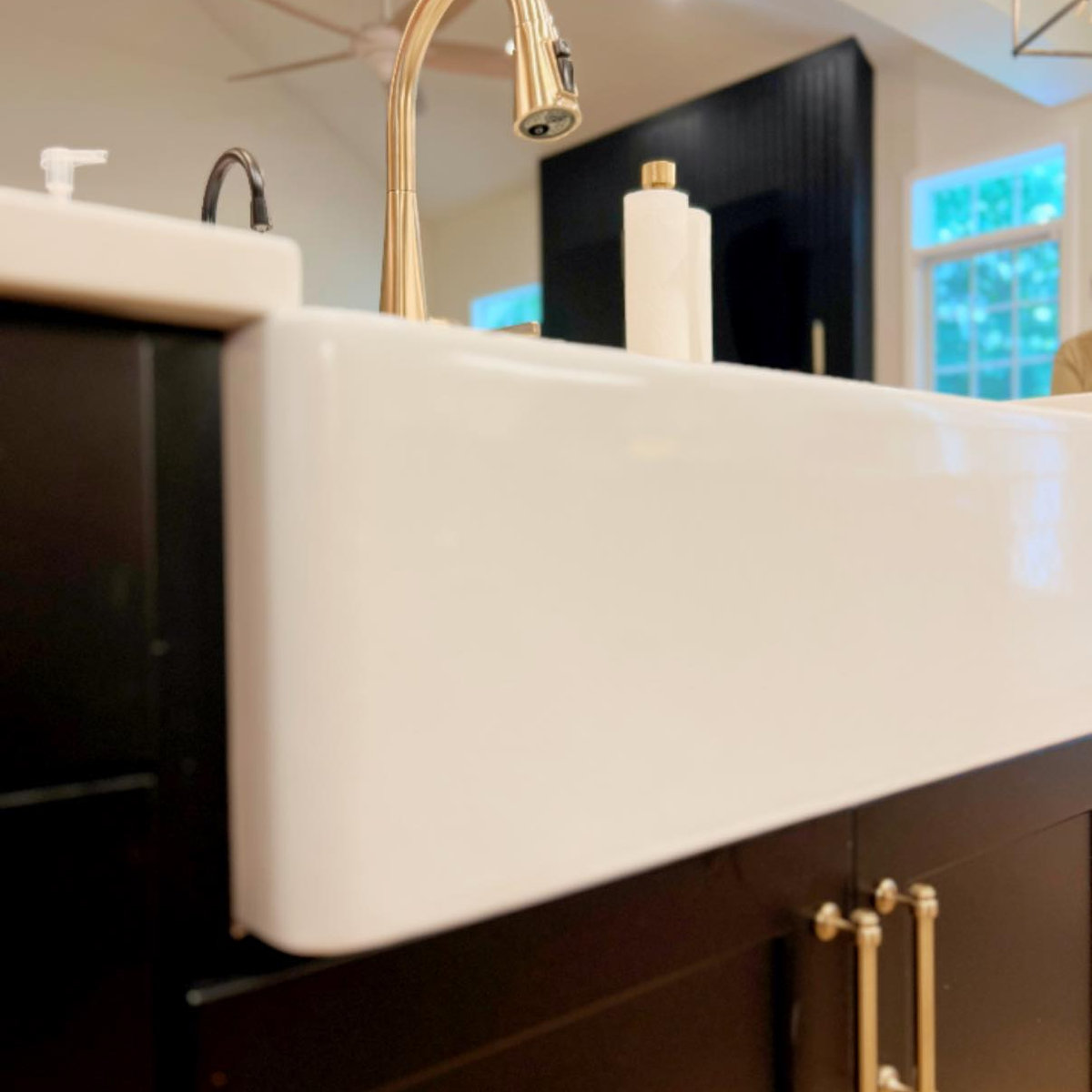 black kitchen cabinets with white farmhouse sink with apron and gold hardware