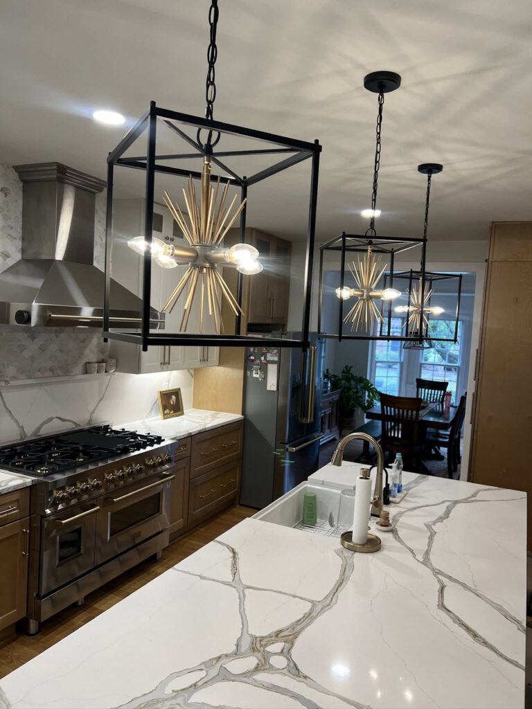 kitchen in davidson, NC that defines functional luxury with bright pendant lighting, stone counters, gold accents, and stainless steel appliances