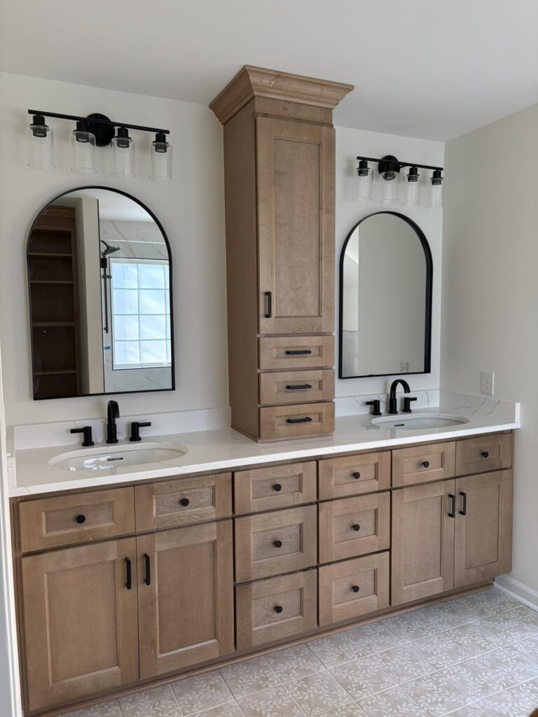 bathroom renovation in Davidson, NC featuring tall central wooden storage between a double vanity with marble countertop.