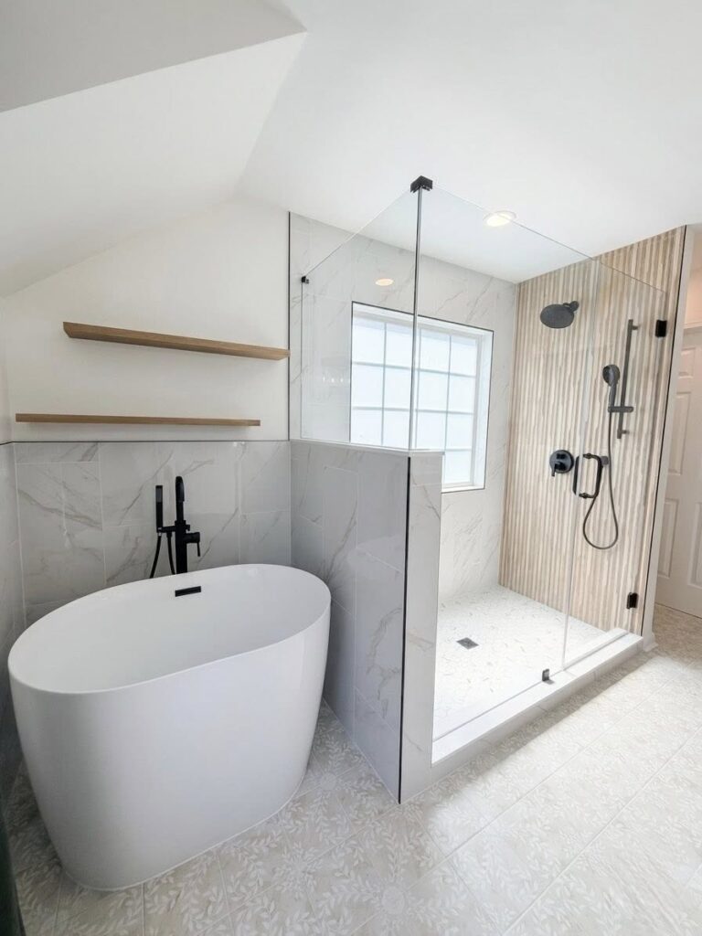Home Renovation near Cornelius, NC features bathroom with whit emarble tiling around a soaking tub, beside walk in glass shower with black faucet