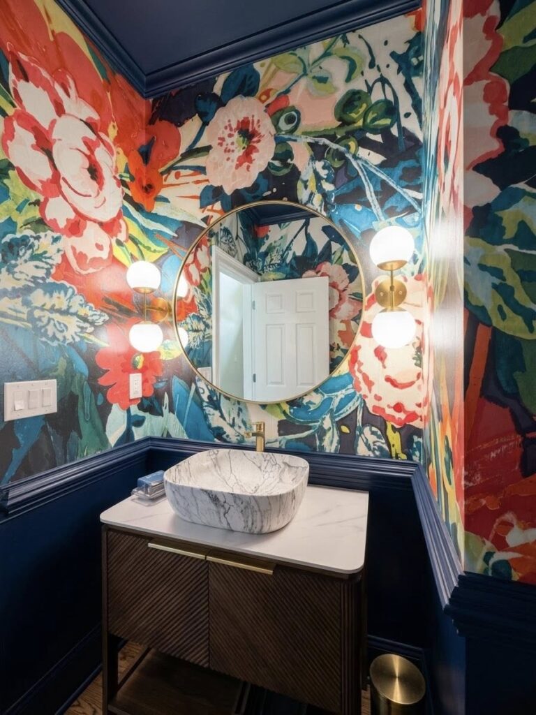 Bold bathroom home renovation near Cornelius, NC with floral wallpaper, blue chair rail molding and blue ceiling above a round mirror. marble sink sits on top of modern cabinet.
