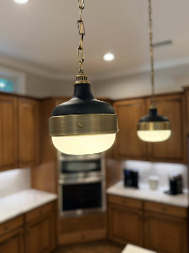 close up on black and bronze pendant lights hanging from a bronze chain in front of warm wood cabinets
