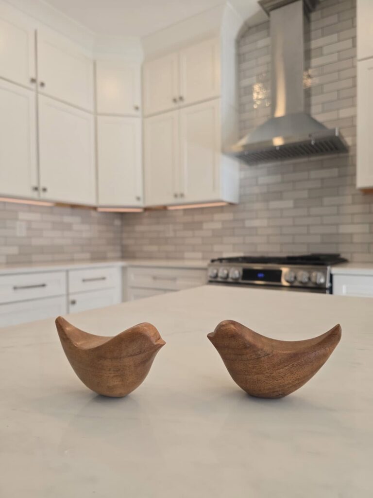 two wooden birds sit on a fresh white kitchen countertop in front of white cabinets and gray tile backsplash of a kitchen renovation near Cornelius, NC.