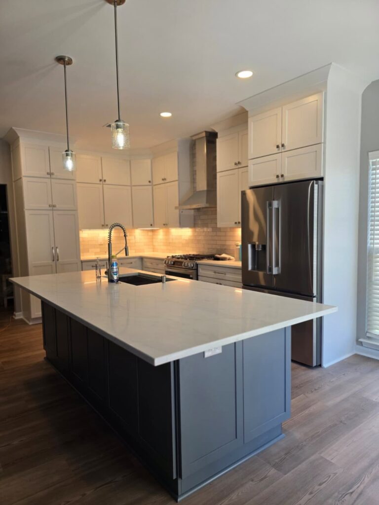 pendant lights hang over a large island in front of white cabinets with under cabinet lighting. recent kitchen renovation featuring home lighting design near Davidson, NC