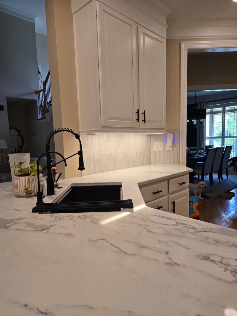 kitchen renovation near Cornelius, NC features white cabinetry with black hardware, a black sink, and marble counters.