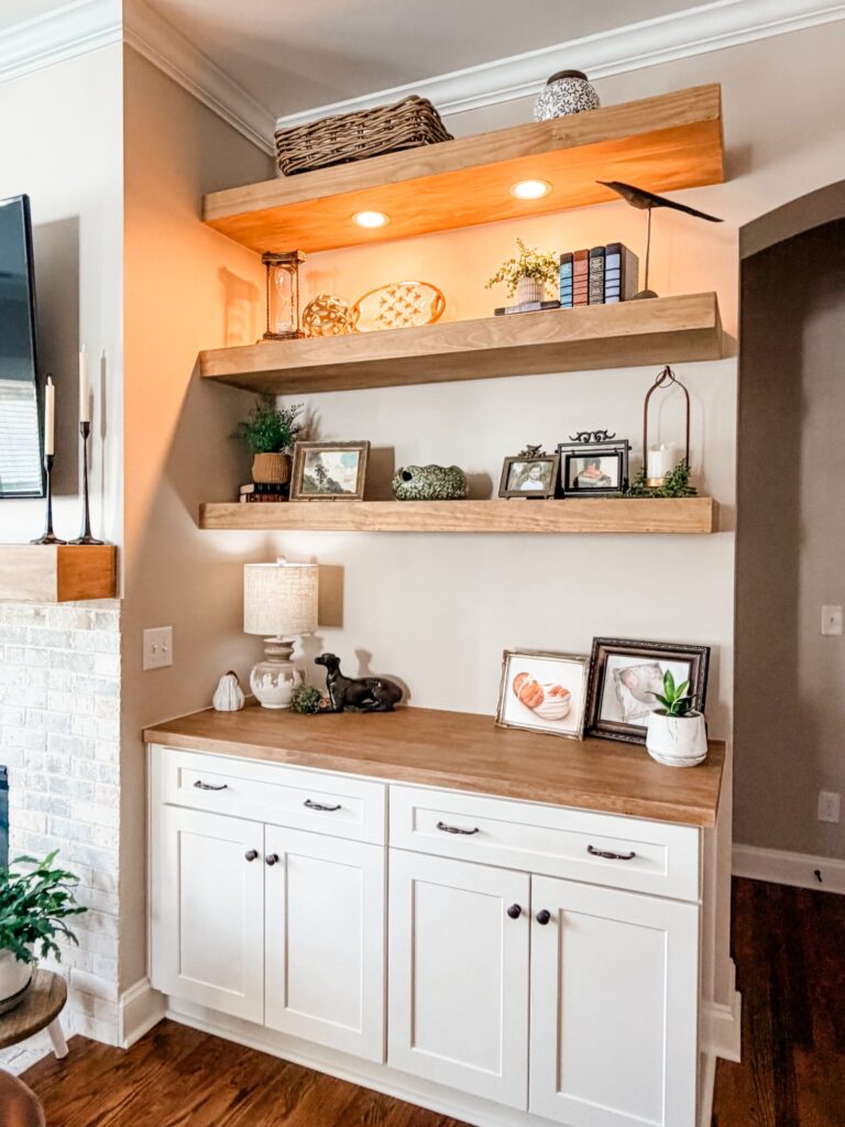 white cabinetry next to a white wash brick fireplace. open wood shelves along the wall above hold books and plants in this custom home renovation near davidson nc