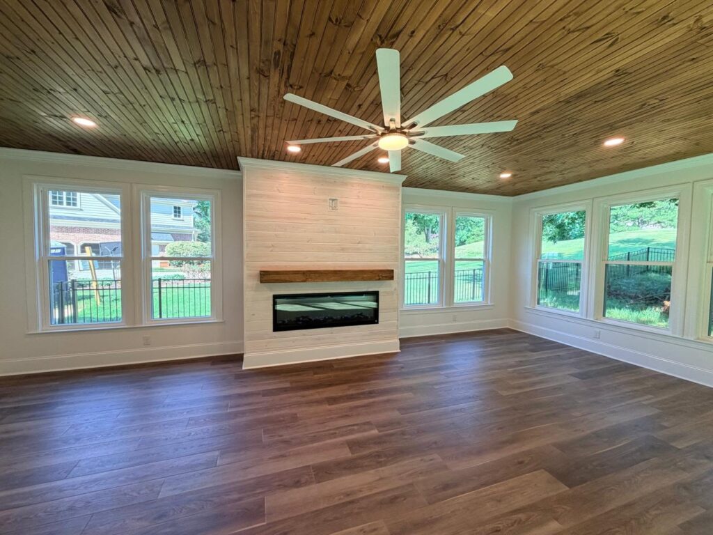 home renovation featuring windows surrounding a shiplap fireplace with minimalist mantle, natural wood ceiling and bright interior near Cornelius, NC.