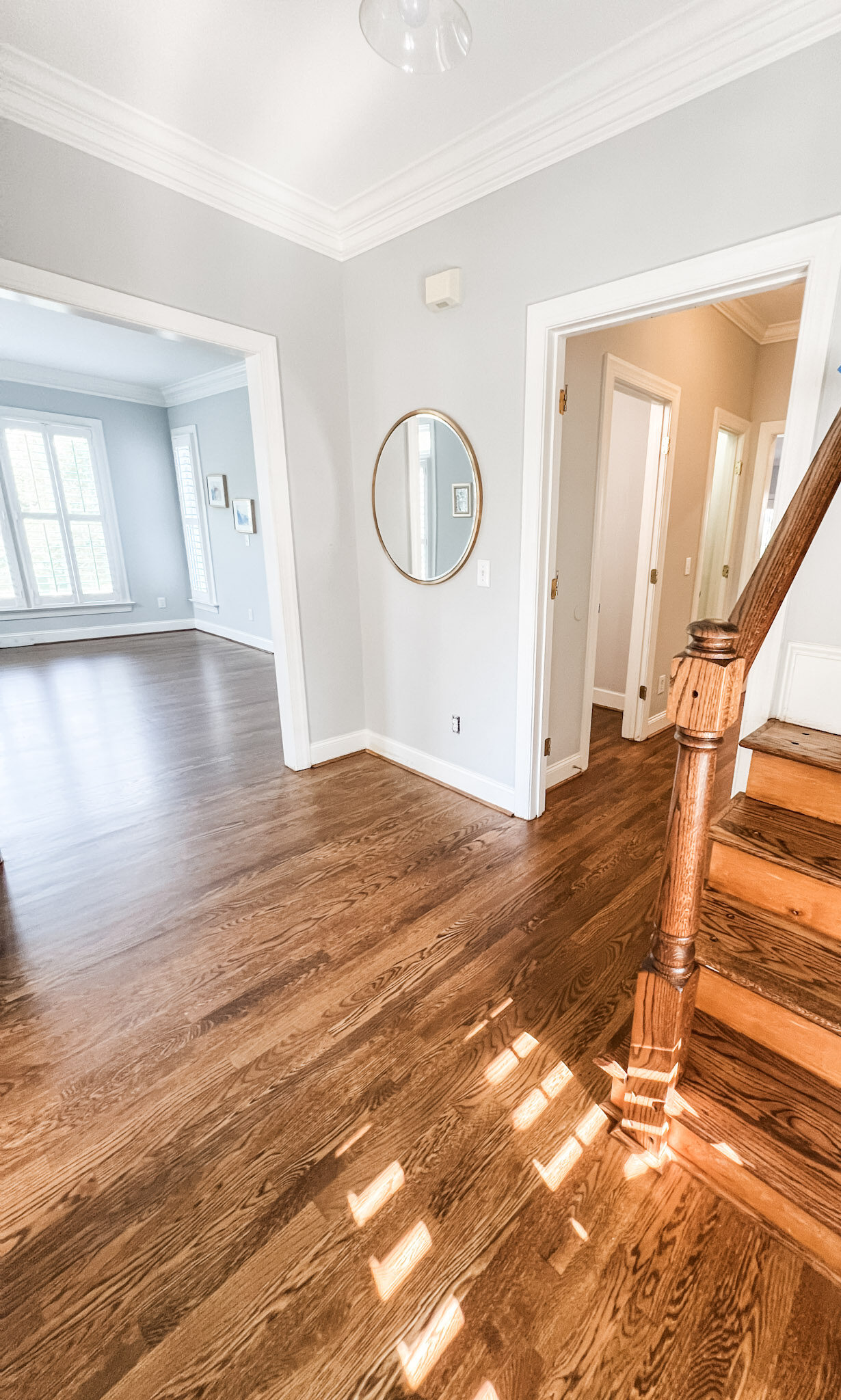 Home flow design improves in between spaces like this small foyer where multiple hallways converge. Stained wood floors contrast with light gray walls with multiple doorways.