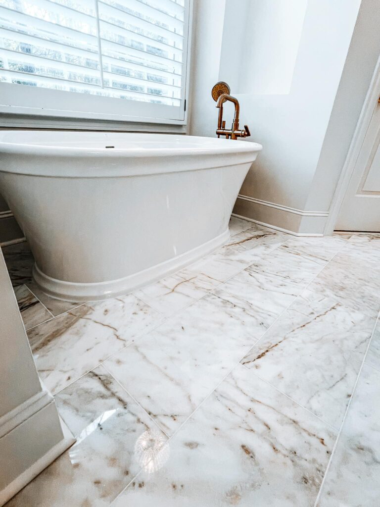 timeless home renovation near Davidson, NC featuring marble flooring, large freestanding white soaking tub, and bronze faucet hardware.