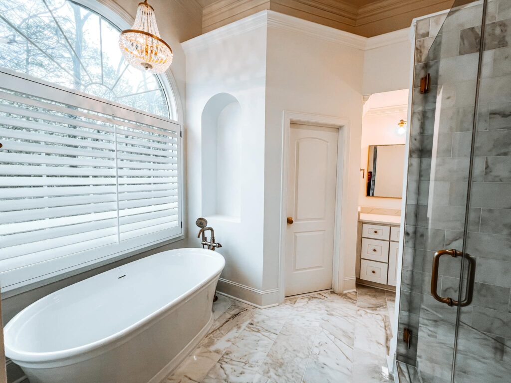 A wider view of the timeless home renovation near Davidson, NC with marble tile flooring, a freestanding soaking tub, marble topped vanities, and glass shower enclosure.