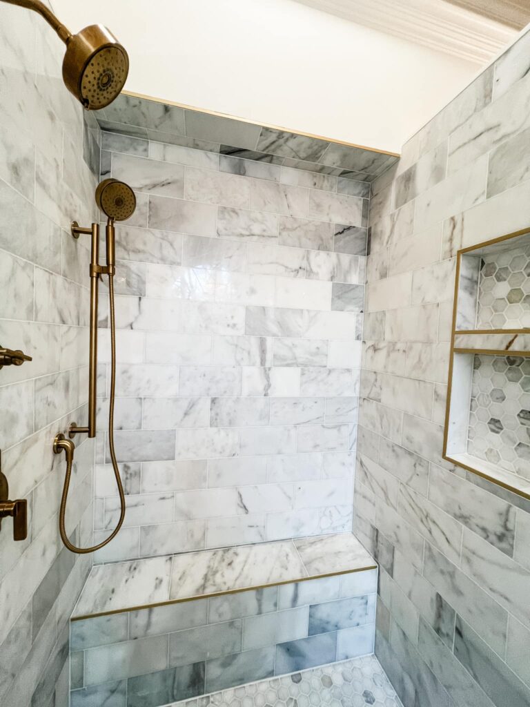 bathroom renovation near Davidson, NC featuring marble tile shower with bronze hardware and inset nook with hex tiling on the right wall.