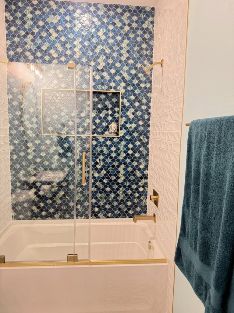 Intentional Design in action in a bathroom renovation featuring unique blue tiles in a practical white shower/tub combo with gold fixtures.