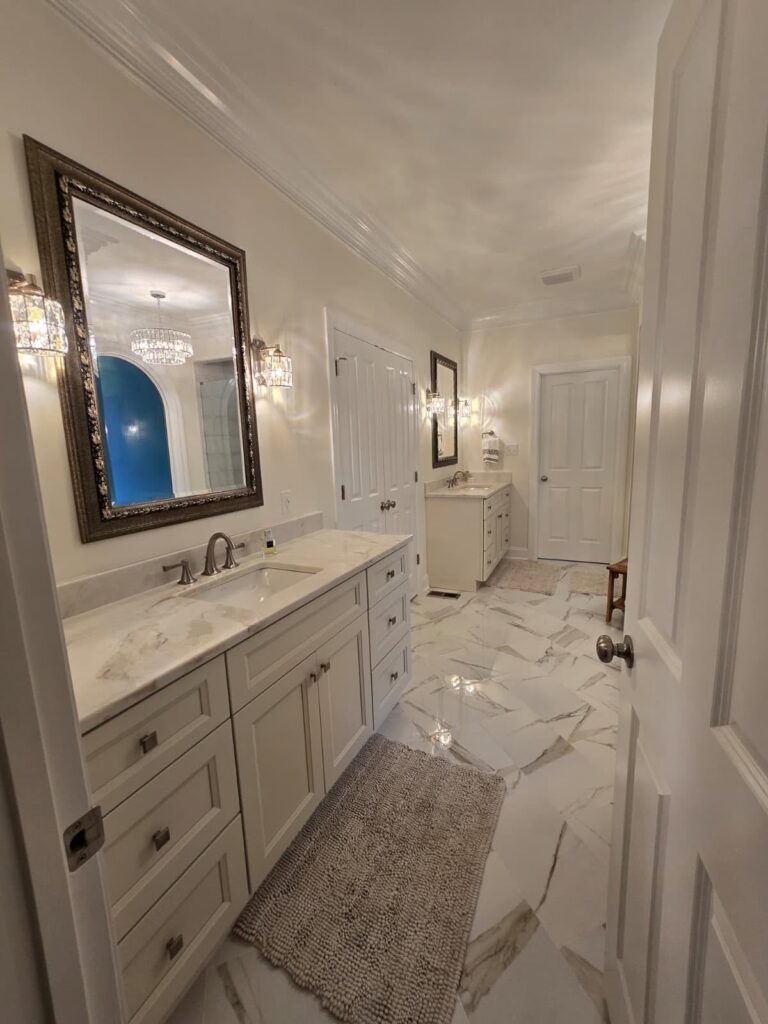 all white bathroom with two vanities on either side of a white double doors. both vanities feature a large mirror centered above the sink with sconces on each side of the mirror