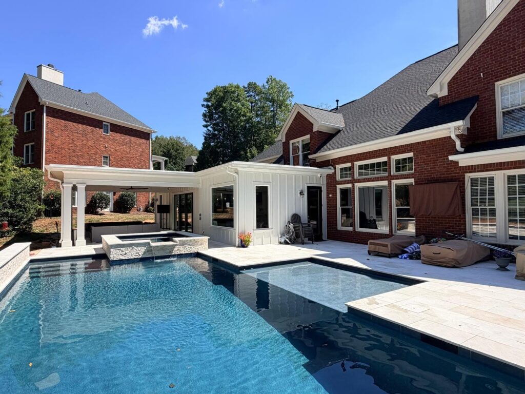 seasonal home design guides this home renovation near cornelius, NC featuring large modern pool, stone decking, covered patio, and enclosed living space connected.
