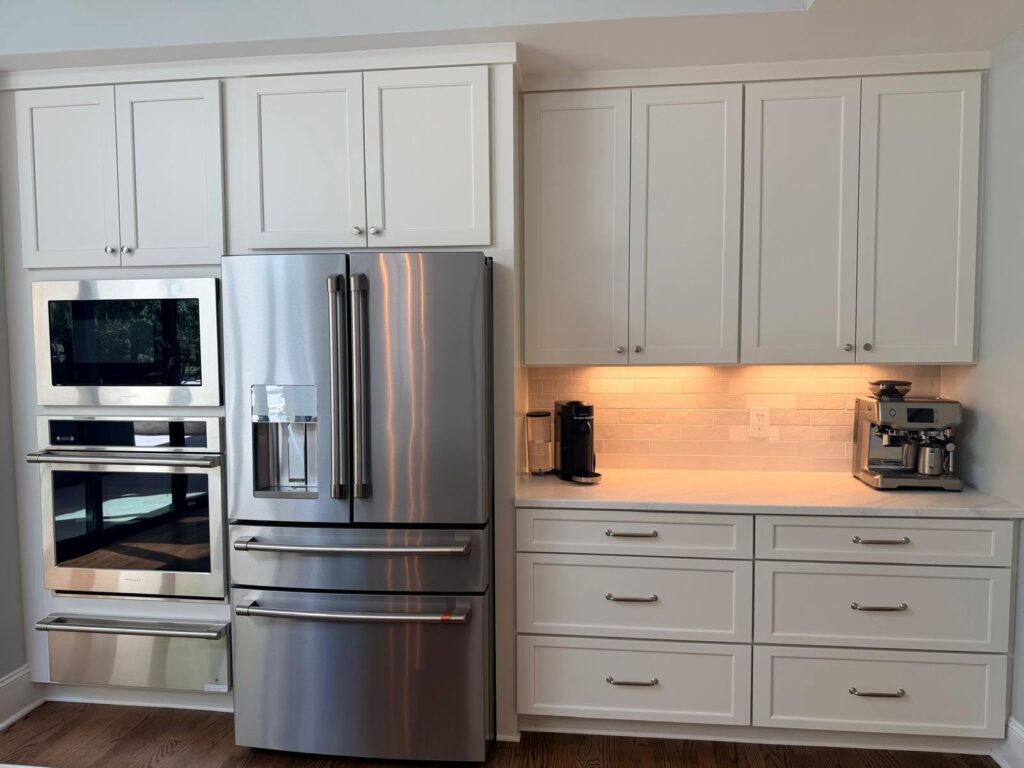 A straight forward kitchen highlights intentional home design with subway tile backsplash, light stone counters, gray cabinetry, and stainless steel appliances.