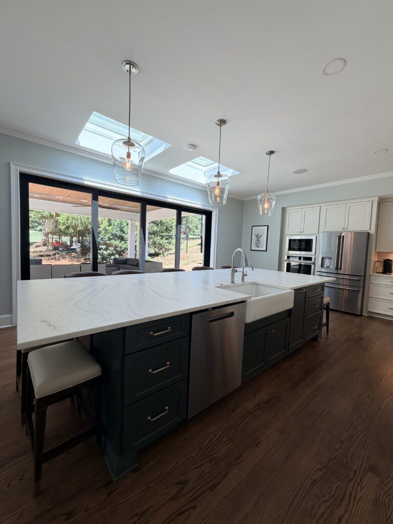 Luxury home remodel featuring large open kitchen with white stone counters, cream cabinetry, and glass pendant lights suspended above the huge central island.